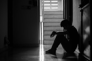 Silhouette of man sitting alone,Sad and Serious Man sitting hug his knee alone of close condo.,...