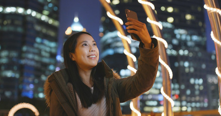 Woman making live stream on cellphone in the city at night, beautiful city building background at night