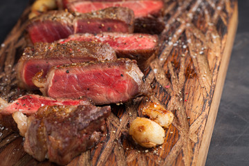 Closeup ready to eat steak new York beef breeds of black Angus with herbs, garlic and butter on a wooden Board. The finished dish for dinner on a dark stone background. Top view