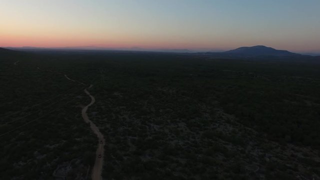 Drone shot of dune buggies driving on offroad on a dirt road in last sunset light