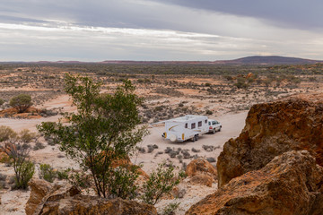 Fototapeta na wymiar Four wheel drive vehicle and large white caravan camped beside ancient red cliffs in the outback of Australia.