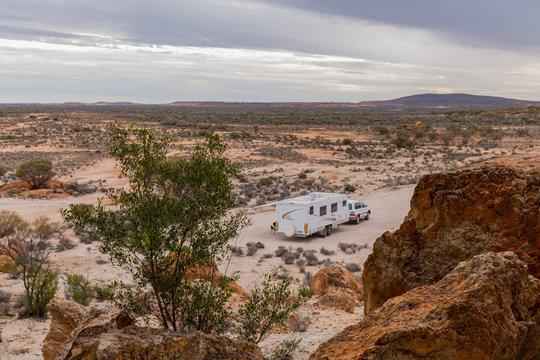 Four wheel drive vehicle and large white caravan camped beside ancient red cliffs in the outback of Australia.