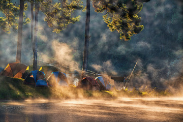 Camping tents under pine trees with sunlight shine , fog flow on lake in the morning at Pang Ung, Mae Hong Son, THAILAND..
