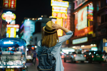 Young asian woman traveler with blue backpack and hipster hat looking night view on road with tuk...