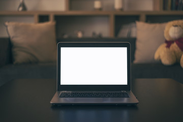 Laptop with white blank mockup screen is on top of wood table with living room background.