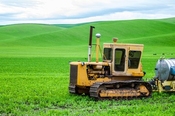Obraz premium A tractor in front of lush green wheat fields in spring