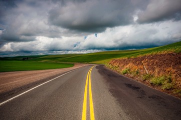 A road through wheat fields with dramatic storm clouds in spring