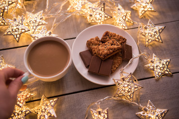 Christmas and new year holiday celebration concept background. Cup of coffee, homemade chocolate cookie and peanut biscuit, lighted candles, xmas tree decoration on wooden table.