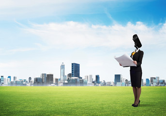 Camera headed woman standing on green grass against modern cityscape