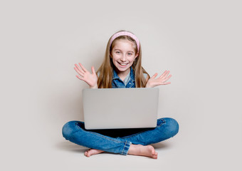 Naklejka premium Cheerful little girl sitting on the floor with laptop