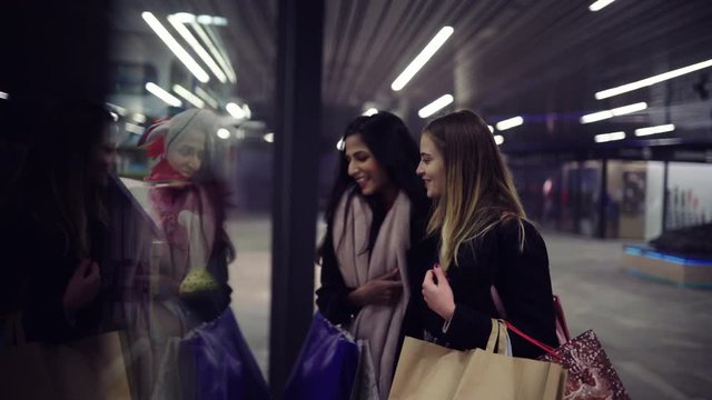 Two cute young adolescent women, heavy loaded with christmas gifts,  shopping, while walking along store windows and choosing and admiring the items. 