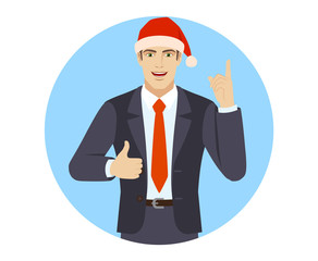 Businessman in Santa hat pointing up and showing thumb up