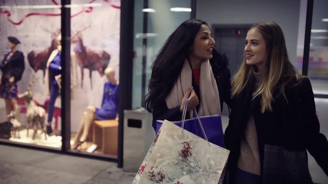 Two cute young adolescent women, heavy loaded with christmas gifts,  shopping, while walking along store windows and choosing and admiring the items. 