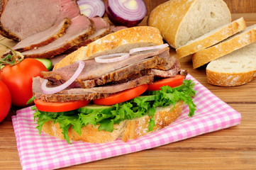 Roast beef salad sandwich with ingredients on a wood background