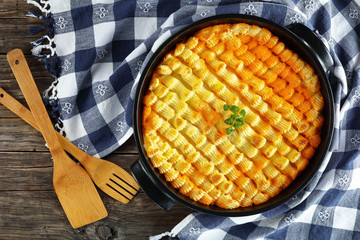 delicious shepherd's pie or cottage meat pie in baking dish on dark wooden table with kitchen towel and wooden spatulas , authentic recipe of english cuisine, horizontal view from above