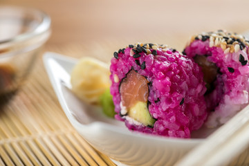 Zwei California Inside Out Sushi mit modern Pink gefärbten Reis, Lachs, Avocado, Frischkäse und Sesam