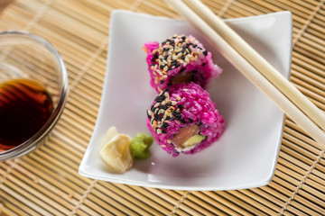 Zwei California Inside Out Sushi mit modern Pink gefärbten Reis, Lachs, Avocado, Frischkäse und Sesam