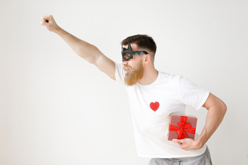 Confident male hero in batman mask, raises hand, hurries to help people, holds present box, going to give it someone, isolated over white background. Bearded man feels himself batman poses indoor