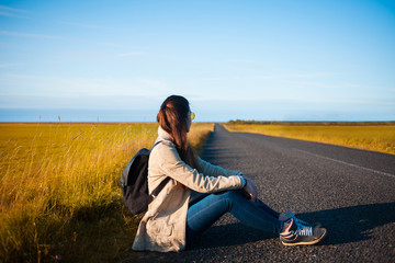Young woman tourist sits on the road.