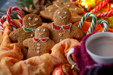 Christmas atmosphere of magic. Gingerbread and hot cocoa in a cup with a cheerful scarf. Funny smiling little men and candy canes.