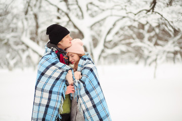 Young couple stays close to each other having checkered plaid on their shoulders.