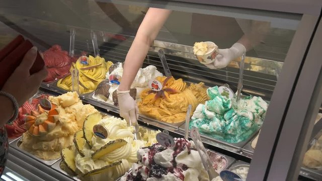 a sales assistant scoops out frozen gelato from a display cabinet in rome, italy