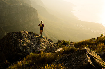 A young lady trail runner watching the sunset from a mountain top on the Cape peninsula of South Africa.  - obrazy, fototapety, plakaty