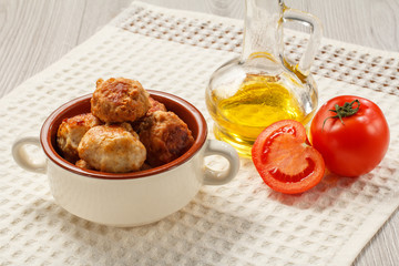 Fried meat cutlets in ceramic soup bowl, red tomatoes and glass bottle with sunflower oil on kitchen towel