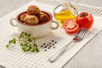 Fried meat cutlets in ceramic soup bowl, red tomatoes, glass bottle with sunflower oil, metal fork, branch of fresh parsley and black peppercorn