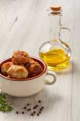 Fototapeta na wymiar Fried meat cutlets in white ceramic soup bowl, glass bottle with sunflower oil, branch of fresh parsley and black peppercorn
