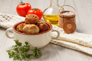 Fried meat cutlets in ceramic soup bowl, red tomatoes, glass bottle with sunflower oil, wooden salt barreled cellar, kitchen towel and branch of fresh parsley