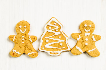 Gingerbread men friends at the Christmas tree on a white wooden table.
