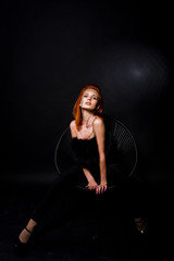Fashion model red haired girl with originally make up like leopard predator isolated on black. Studio portrait on chair.