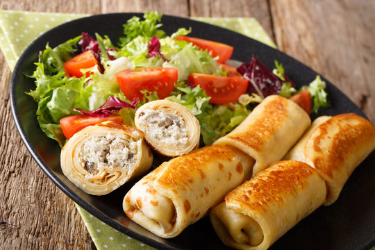 Tasty food: crepes rolls with chicken and mushrooms and vegetable salad on a plate close-up. horizontal