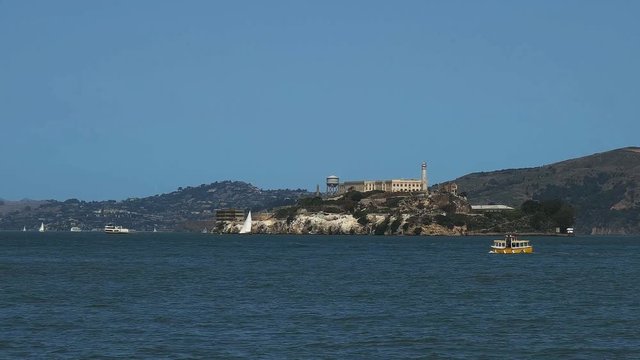 a cute small yellow ferry sails past alcatraz island in san francisco, california