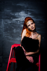 Fashion model red haired girl with originally make up like leopard predator against steel wall. Studio portrait on ladder.