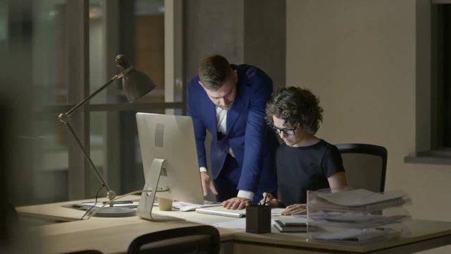 Businessman discussing documents with female colleague while working late in the office