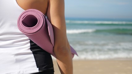 Woman in sport suite carry pink training mattress on the beach