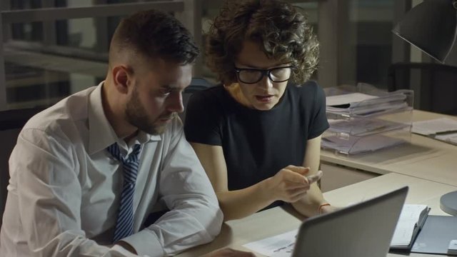 Businesswoman taking document and discussing it with male colleague while working at night