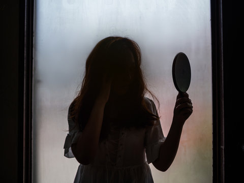 Ghost girl holding mirror standing in front of window