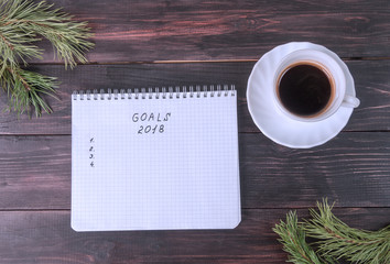 Notepad with plans for the new year, white mug with coffee on a wooden background and fir branches