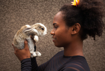 Idealistic young afro american woman daydreaming with Easter bunny rabbit in her hands, feeling...