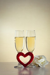 Two glasses with champagne, a red heart handmade and a white rose flower