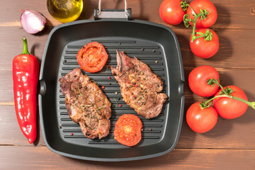 Grilled steak on grill pan with tomatoes on dark background