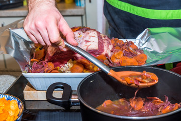 Male hand spraying cooked vegetables with sauce over raw beef rib steak for roasting