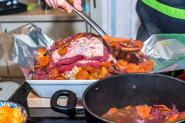 Male hand spraying cooked vegetables with sauce over raw beef rib steak for roasting