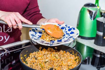 Female hands placing cooked buckweat portions to colorful plates over modern electric cooker in kitchen