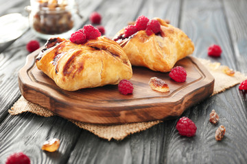 Board with delicious puff pastries and raspberries on table