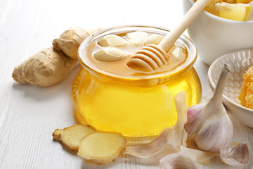 Glass jar with honey and garlic on white wooden table, closeup