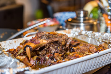 Roasted beef rib steak with bone in roasting tray on busy kitchen table